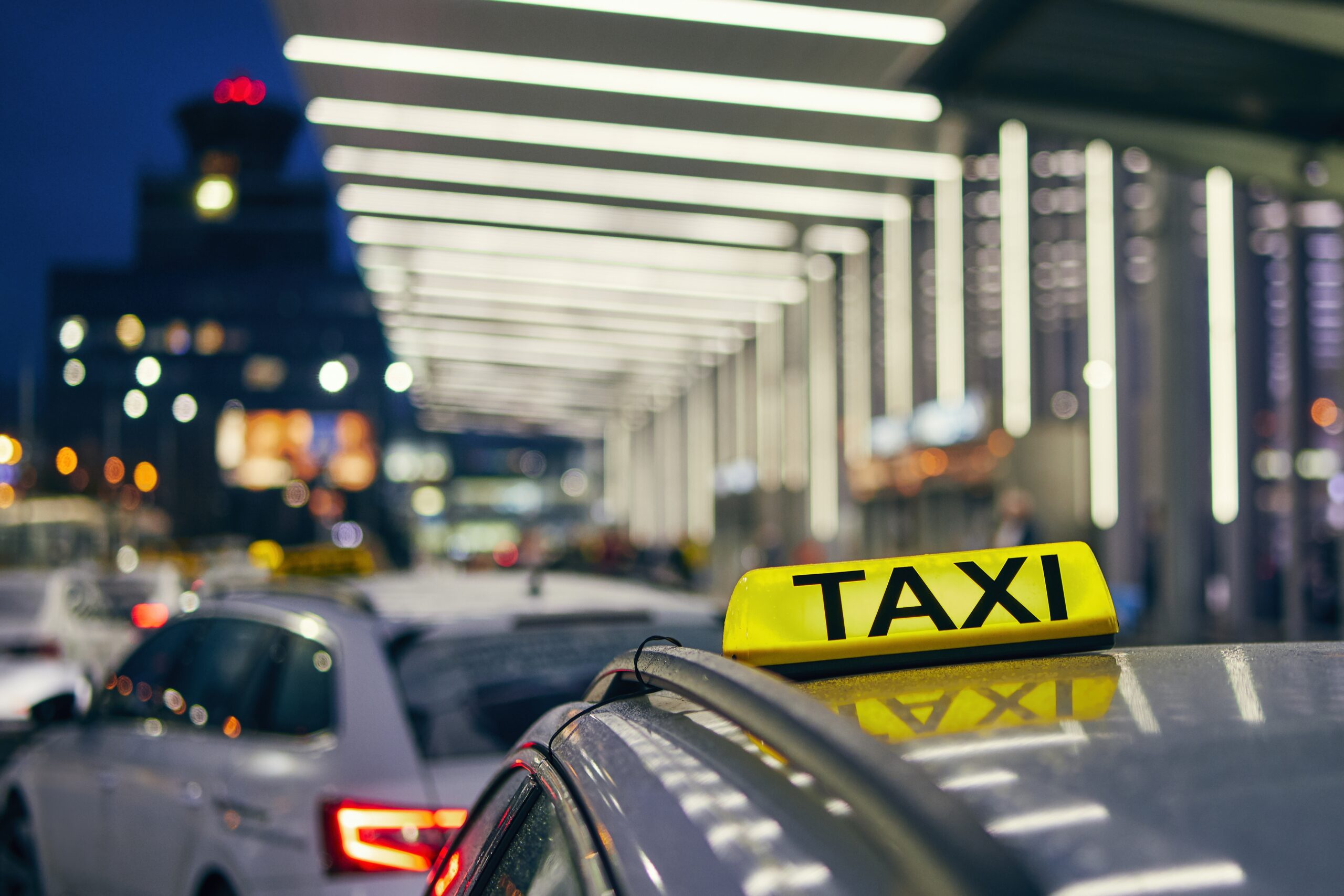 Lighting taxi sign on the roof of car against airport terminal at night.