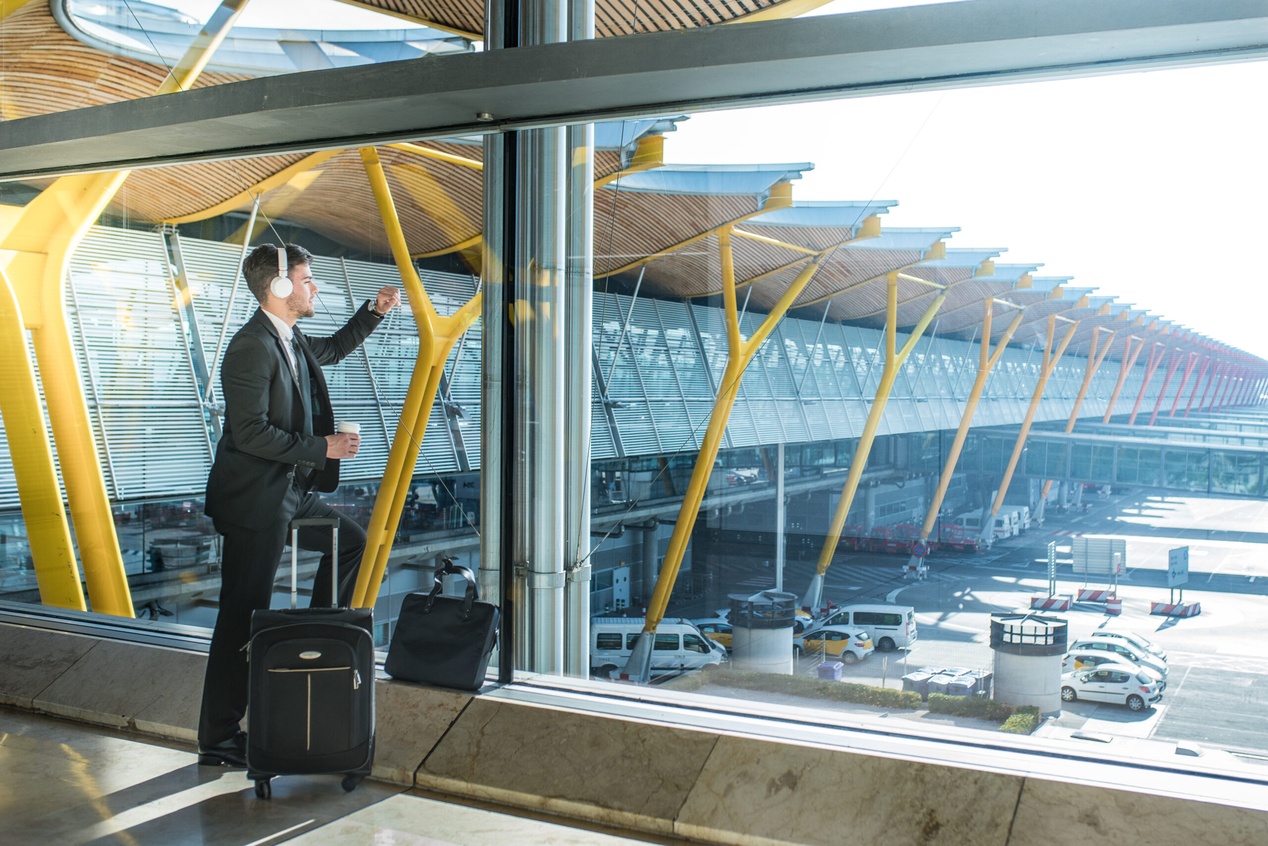 young businessman looking through the window listening music at the airport waiting for his flight
